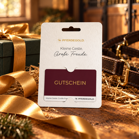 Ein burgunderroter Pferdegold®-Gutschein in einem Displayhalter auf einer Holzunterlage mit Schleife.