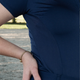 Jemand im Freien, bekleidet mit dem Baselayer Short Sleeve – marineblau von EquiAttire, die Hand in die Hüfte gestützt, mit einem goldenen Armband.